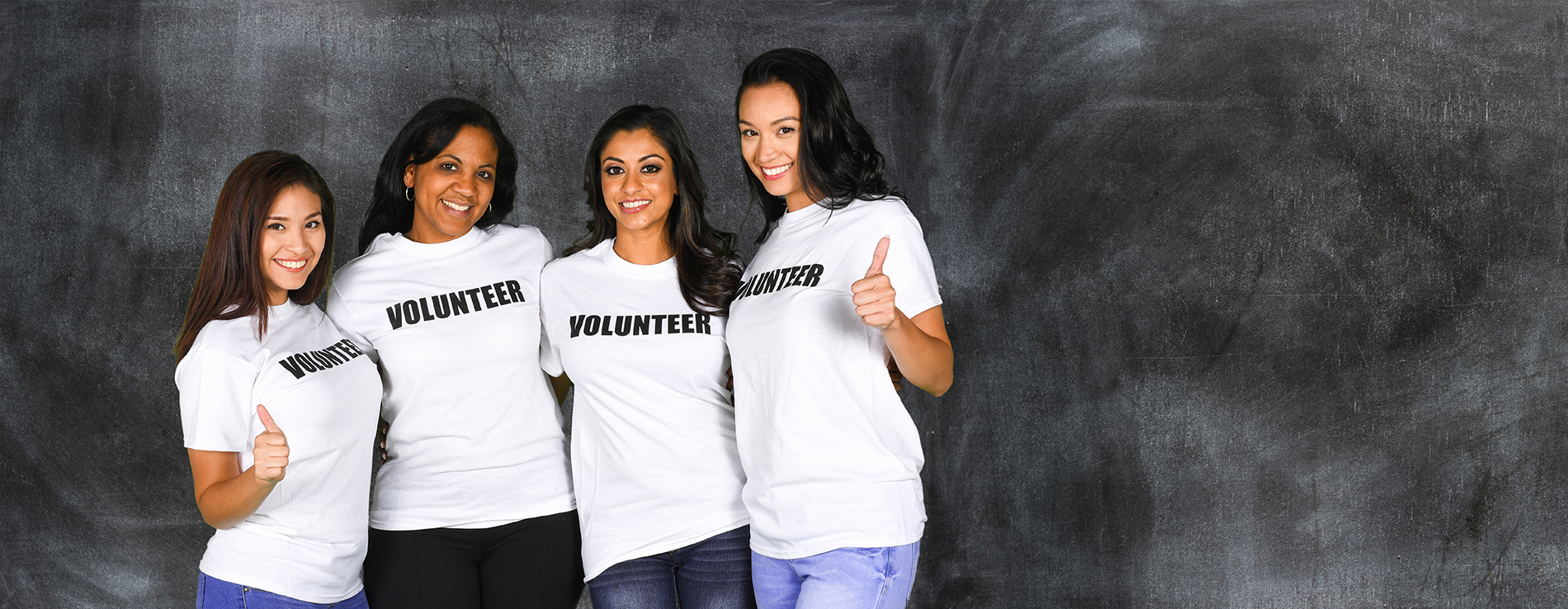 Four girls smiling in white t-shirts that say VOLUNTEER
